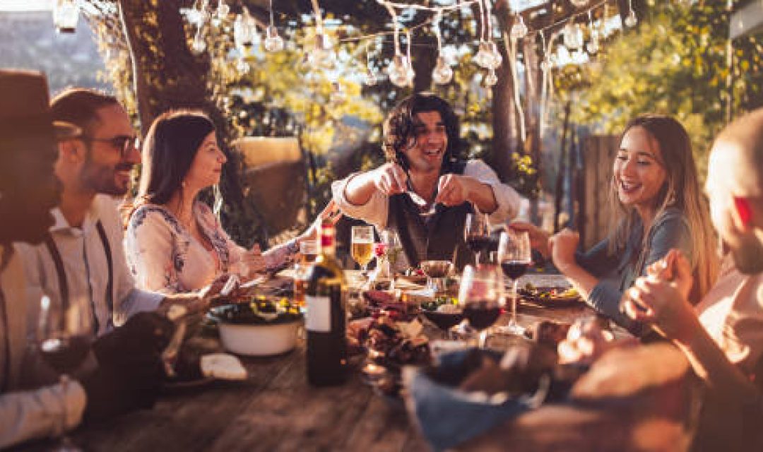 Young elegant multi-ethnic friends celebrating and having mediterranean lunch at rustic countryside mountain village house