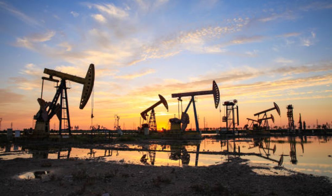 Oil field site, in the evening, oil pumps are running, The oil pump and the beautiful sunset reflected in the water, the silhouette of the beam pumping unit in the evening.