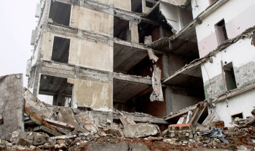 The remains of the destroyed building in the form of piles and a blockage of a pile of stones on the background of a high destroyed structure in a foggy haze. The impact of the destruction. Background