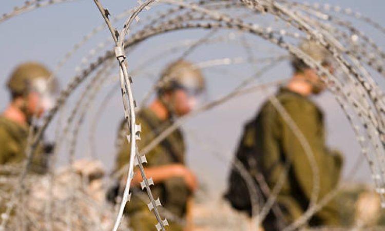 Three Israeli soldiers walk near razor wire near the Palestinian village of Bil'in in the West Bank.