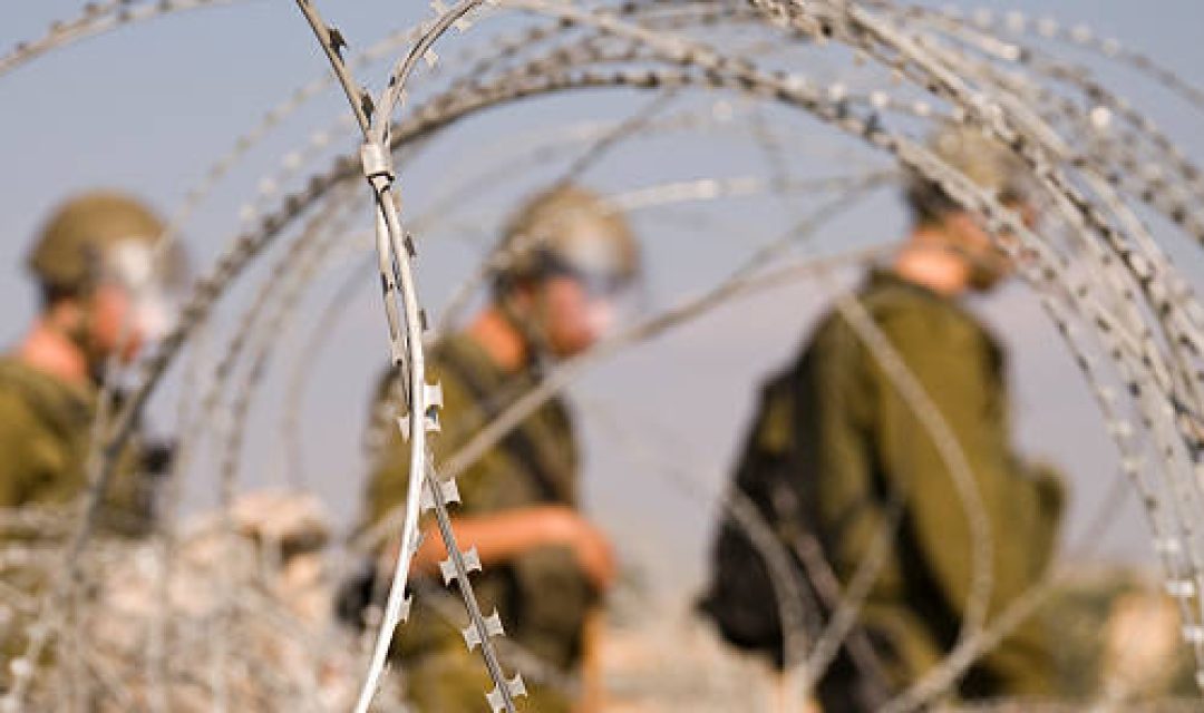 Three Israeli soldiers walk near razor wire near the Palestinian village of Bil'in in the West Bank.