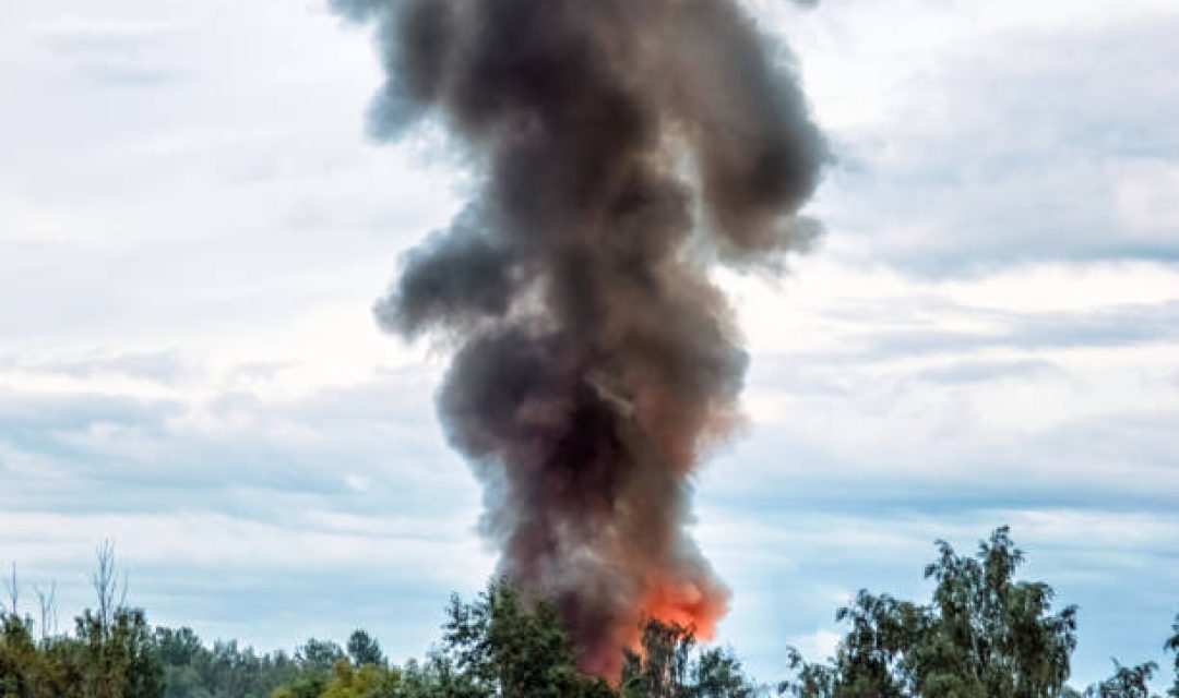 the building burns with fire and black smoke against the evening sky.