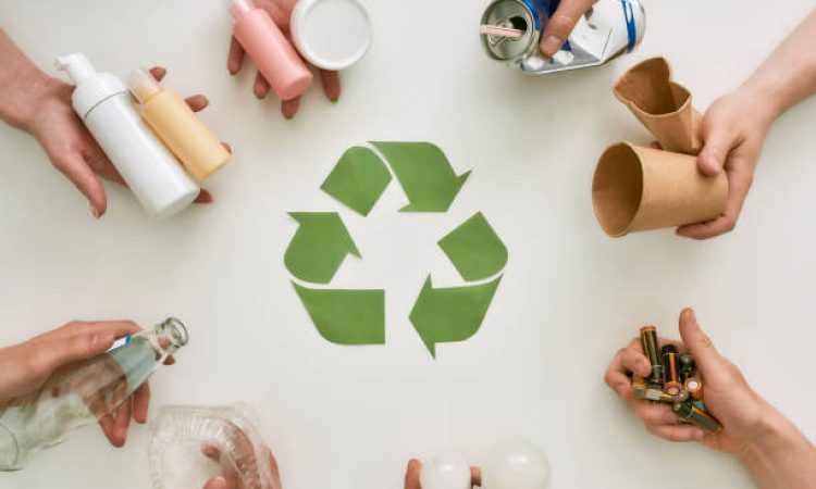 Top view of many hands holding different waste, garbage types with recycling sign made of paper in the center over white background. Sorting, recycling waste concept. Horizontal shot. Top view