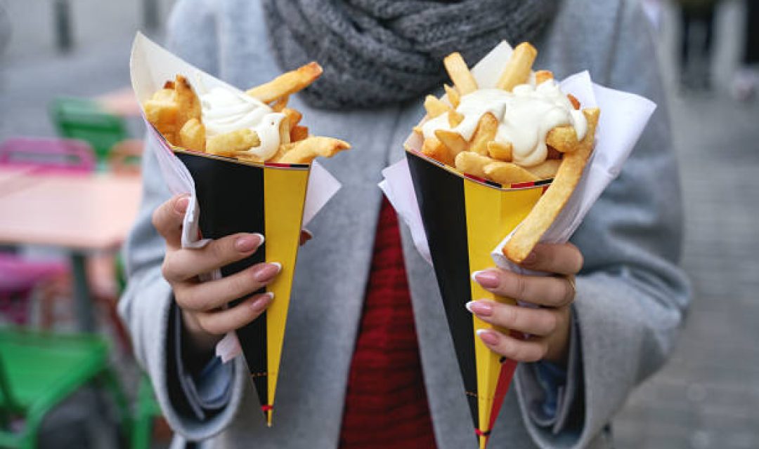 Belgian frites with mayonnaise in Brussels, Belgium. Tourist holds two portions of fries in hands in the street.