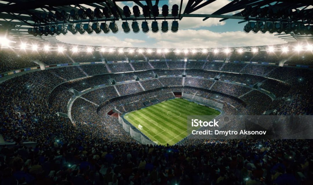 View from the upper tribunes to the soccer stadium full of spectators and lenseflares.